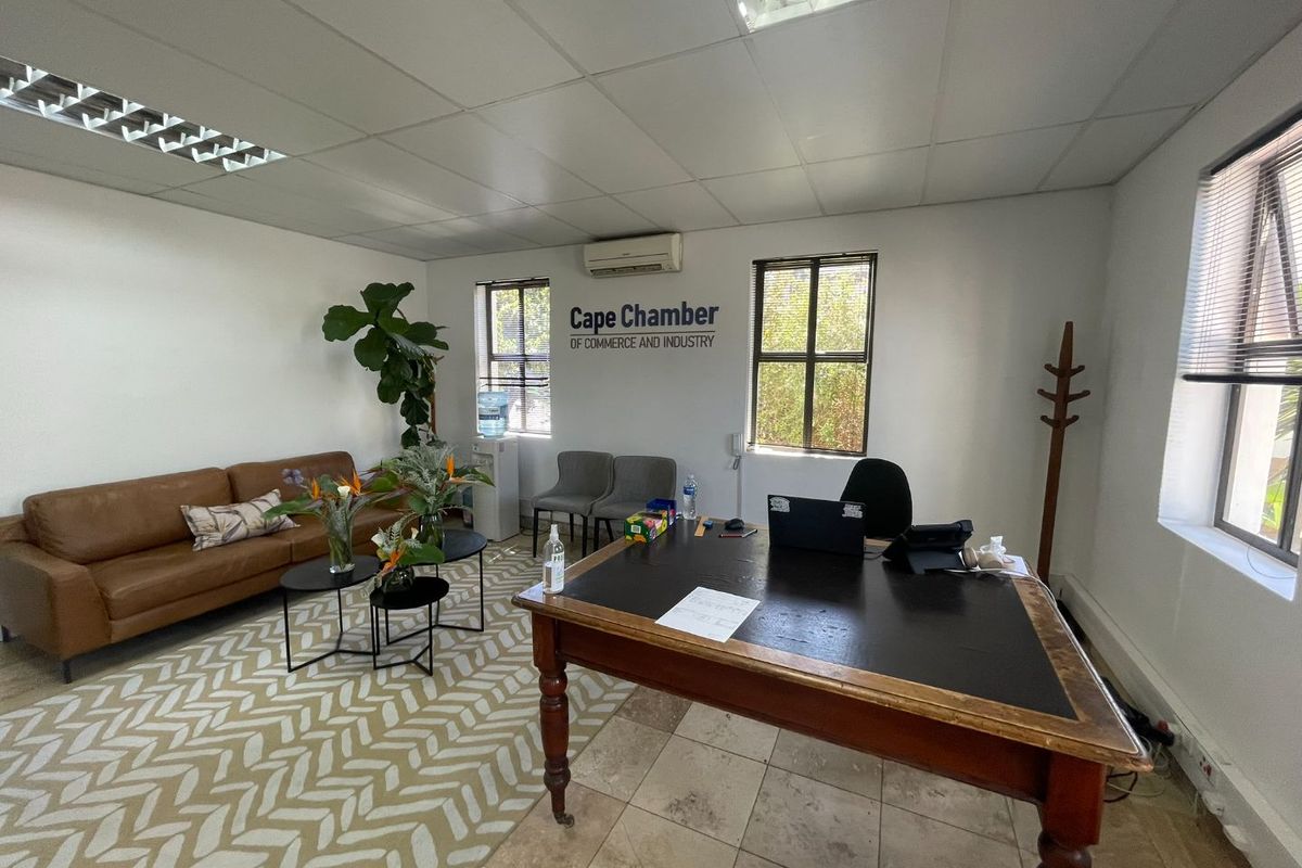 A functional office space featuring tiled flooring, suspended ceiling with recessed lighting, and a wall-mounted air conditioning unit.