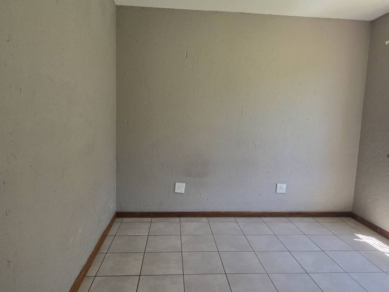 An empty bedroom featuring tiled flooring, security bars on the window, and neutral wall finishes, providing a blank canvas for personalization.