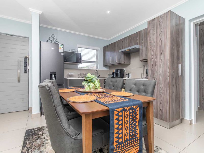 Modern open-plan kitchen and dining area featuring contemporary wood-grain cabinetry, tiled flooring, and integrated fixtures in a well-maintained apartment setting.