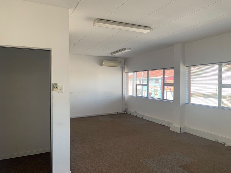 An empty office space featuring carpeted flooring, suspended ceilings, wall-mounted air conditioning, and large windows with venetian blinds.