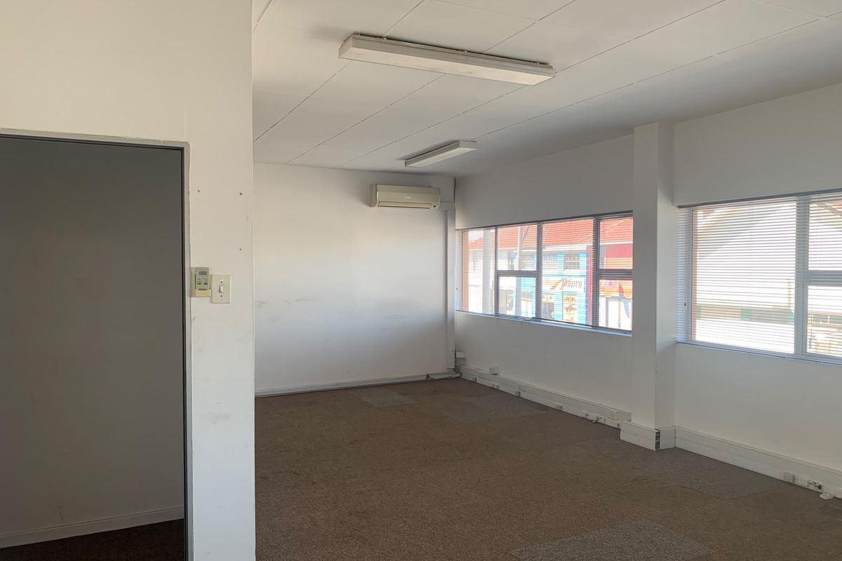 An empty office space featuring carpeted flooring, suspended ceilings, wall-mounted air conditioning, and large windows with venetian blinds.