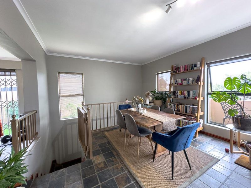 A dining area featuring slate tile flooring, a staircase balustrade, and large windows providing natural light.