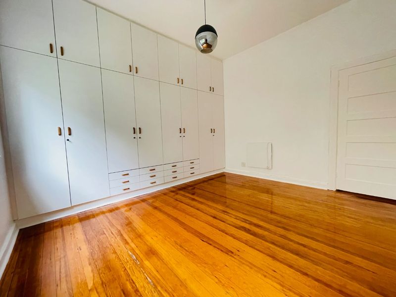 A bright, empty bedroom featuring polished hardwood floors, extensive floor-to-ceiling built-in cabinetry, and a classic panel door.