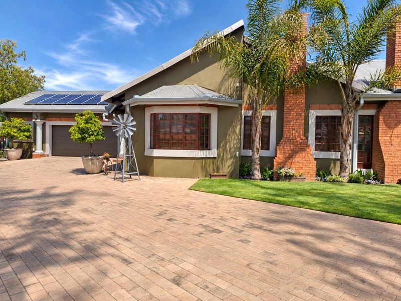 Front elevation of a well-maintained house featuring a paved driveway, solar panels, brick chimney, and a prominent bay window.