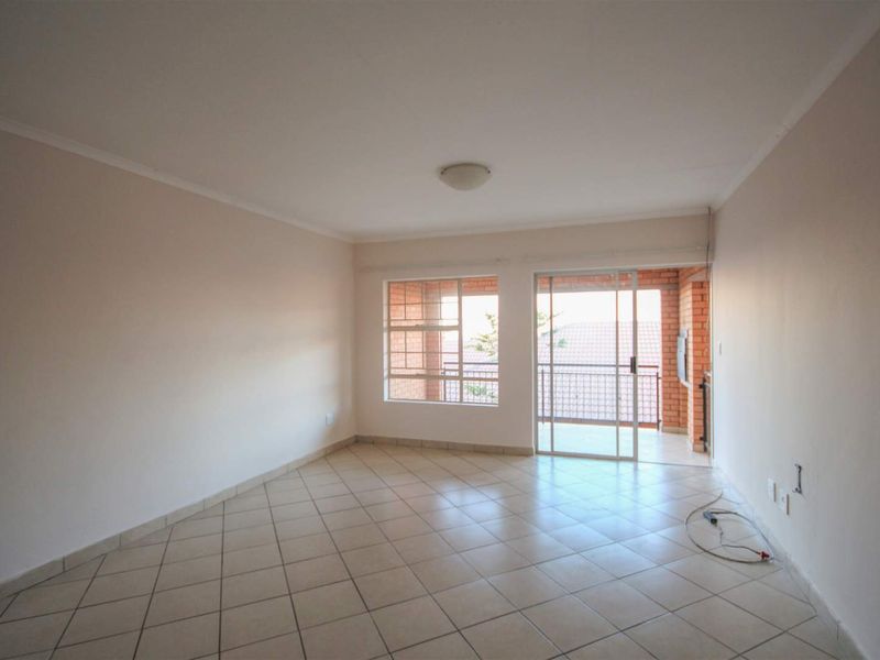 An empty, well-lit living room featuring neutral tiled flooring and direct access to an outdoor balcony through a sliding glass door.