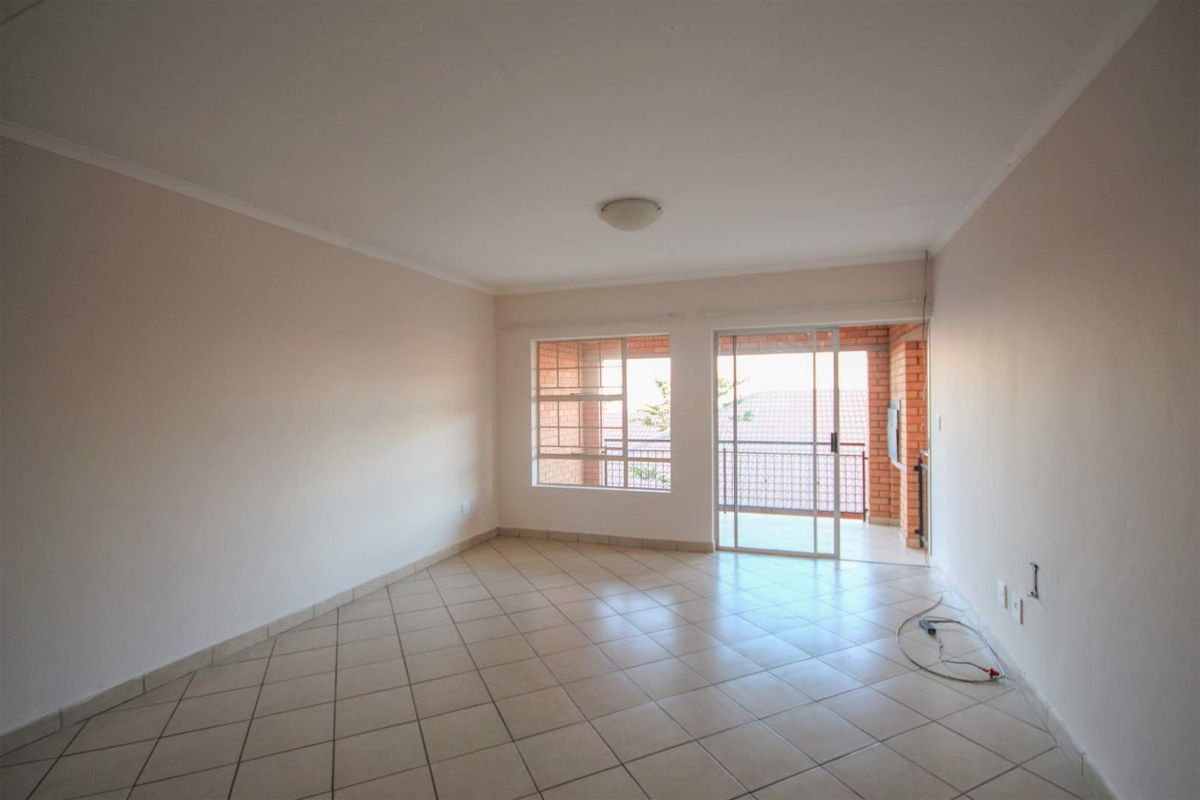 An empty, well-lit living room featuring neutral tiled flooring and direct access to an outdoor balcony through a sliding glass door.
