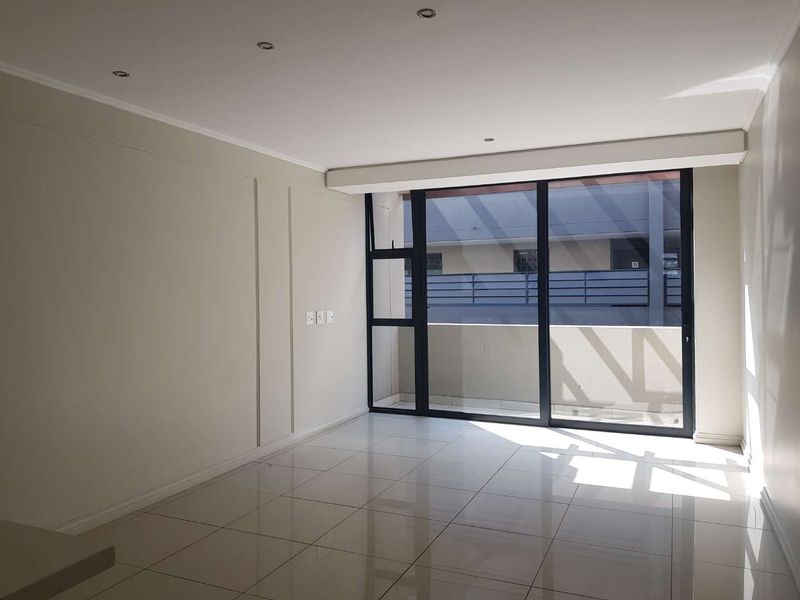 A bright, empty living room featuring neutral walls, polished tile flooring, recessed lighting, and a large sliding glass door leading to a private balcony.