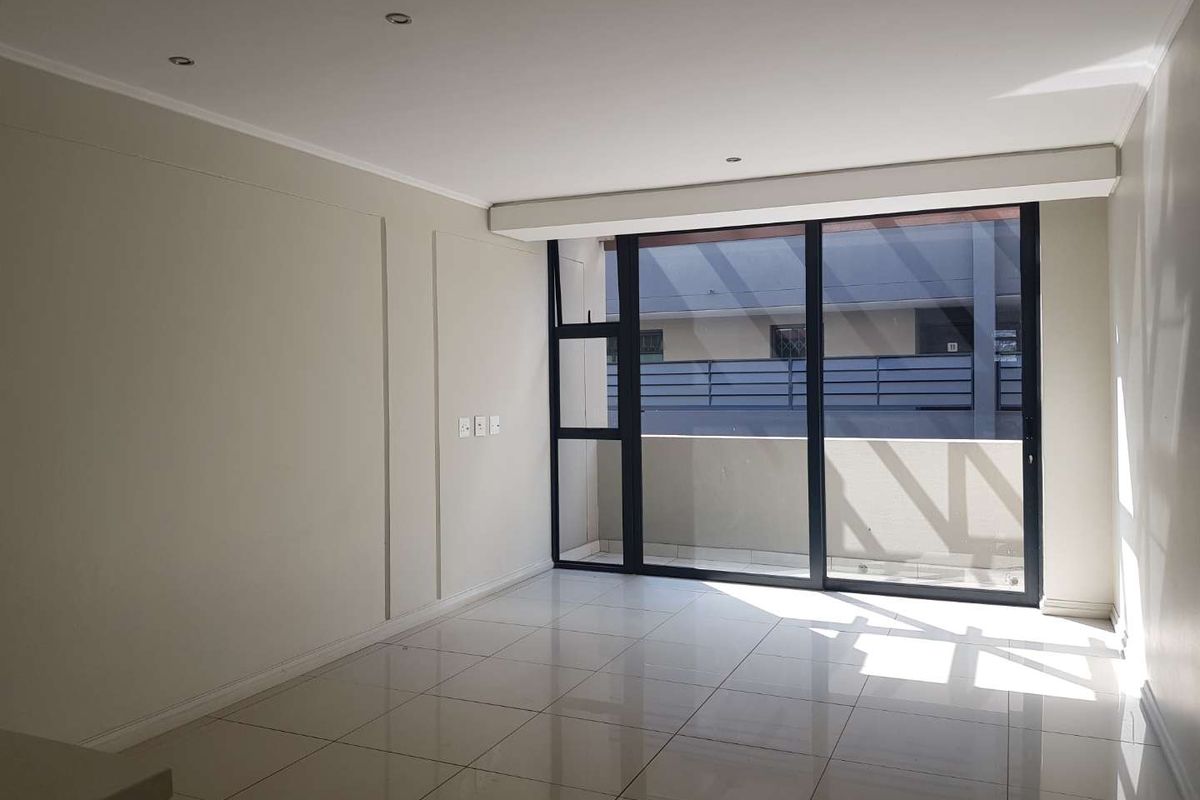 A bright, empty living room featuring neutral walls, polished tile flooring, recessed lighting, and a large sliding glass door leading to a private balcony.