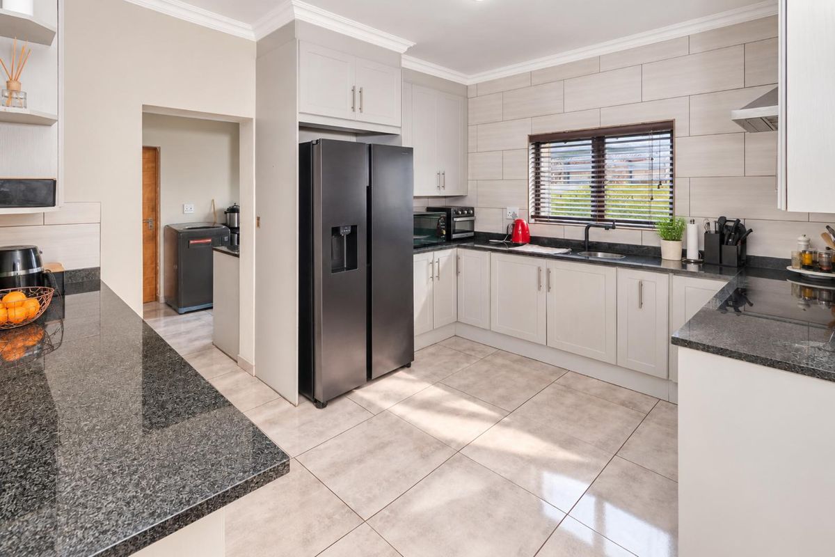 Modern kitchen featuring granite countertops, ample built-in cabinetry, tiled backsplash, and a functional layout with an adjacent scullery area.