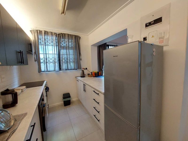 A functional kitchen featuring modern dark and white cabinetry, light countertops, an electric hob, and a window fitted with a security gate.