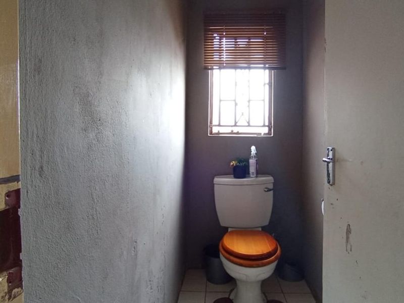 A small, unfinished bathroom featuring a standard toilet, tiled flooring, and a window with security bars.