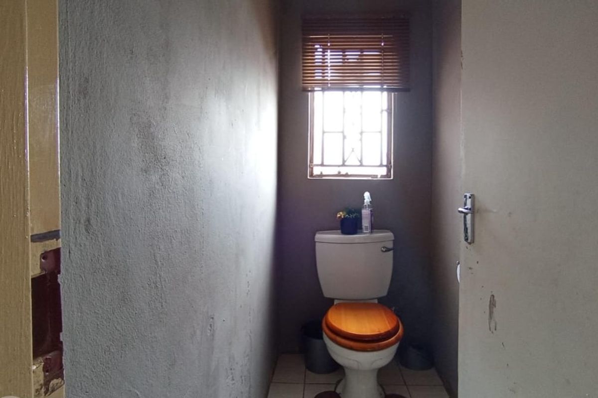 A small, unfinished bathroom featuring a standard toilet, tiled flooring, and a window with security bars.