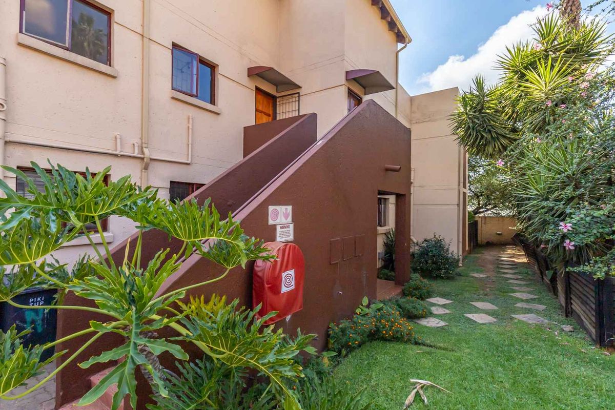 Rear exterior view of the townhouse featuring a concrete staircase, fire safety equipment, and a landscaped garden path.