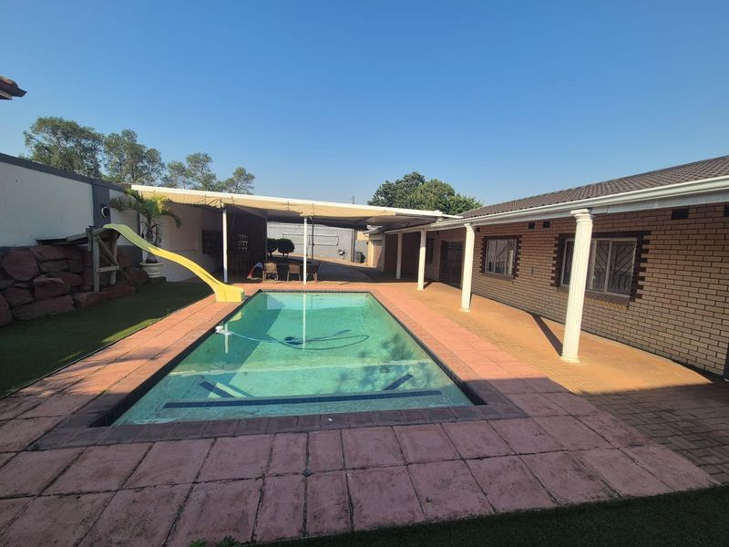 Outdoor pool area featuring a swimming pool with a slide, adjacent covered patio, and brick exterior walls.