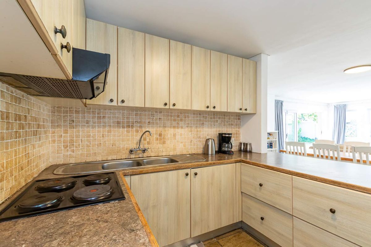 Functional kitchen featuring light wood-look cabinetry, stone mosaic backsplash, integrated electric hob, and a double bowl sink with a breakfast bar extension.