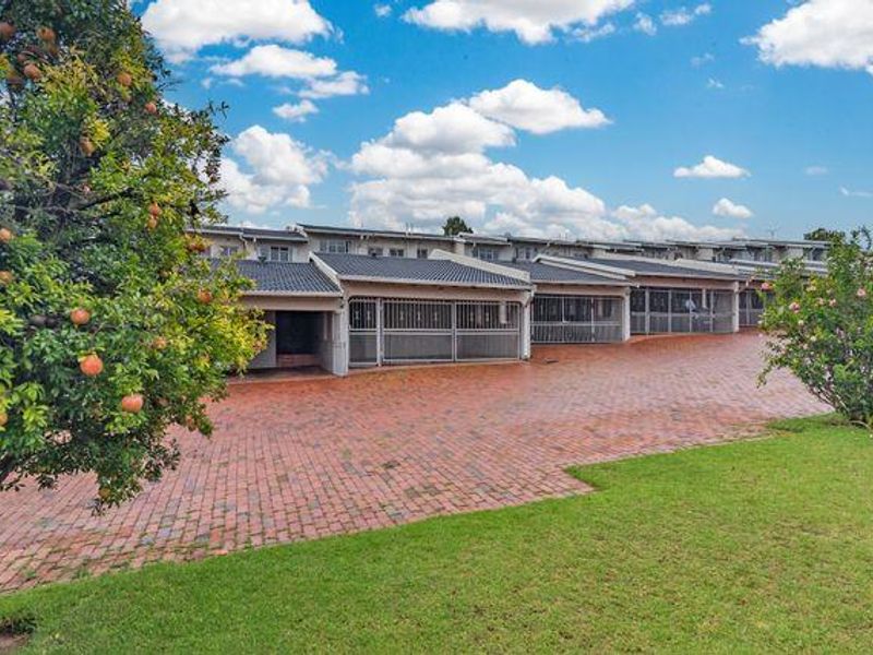 A view of the townhouse complex exterior featuring a brick paved driveway, manicured lawn, and secure unit entrances with tiled roofing.