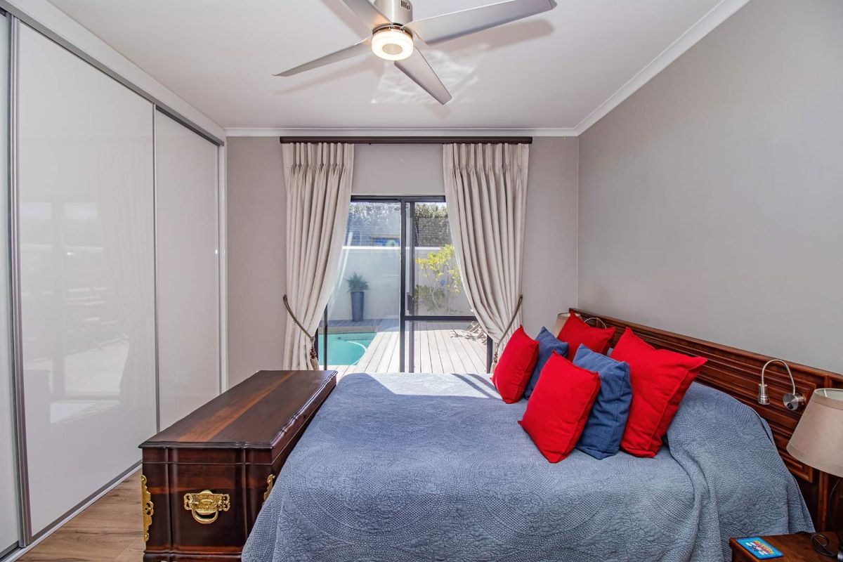 A well-maintained bedroom featuring built-in sliding door wardrobes, a modern ceiling fan, and sliding glass doors providing direct access to the pool area.