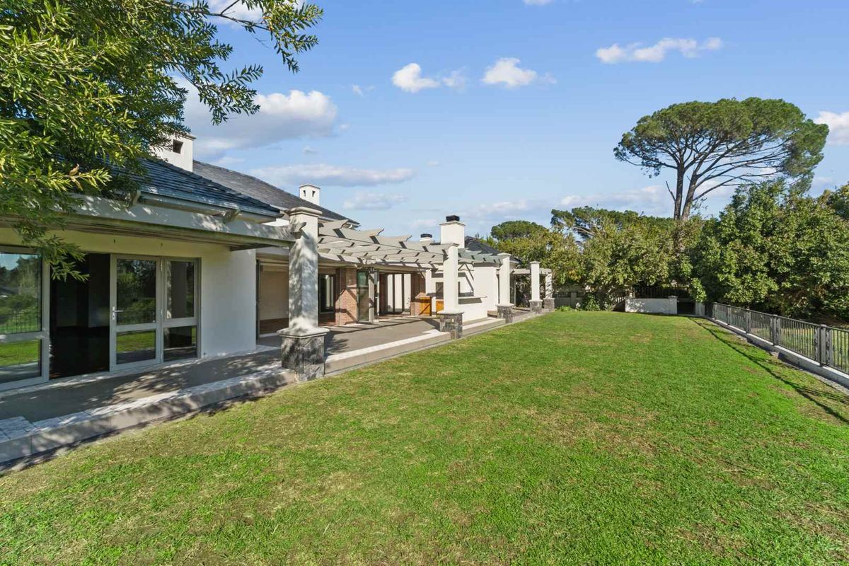 Spacious rear garden featuring a large covered patio with stone-clad pillars, timber pergola, and direct access to the home through sliding glass doors.