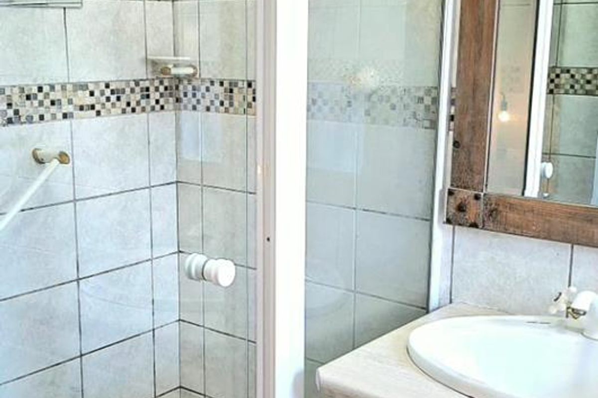A functional bathroom featuring a shower enclosure with a rain shower head, a vanity cabinet with a drop-in sink, and tiled wall finishes.