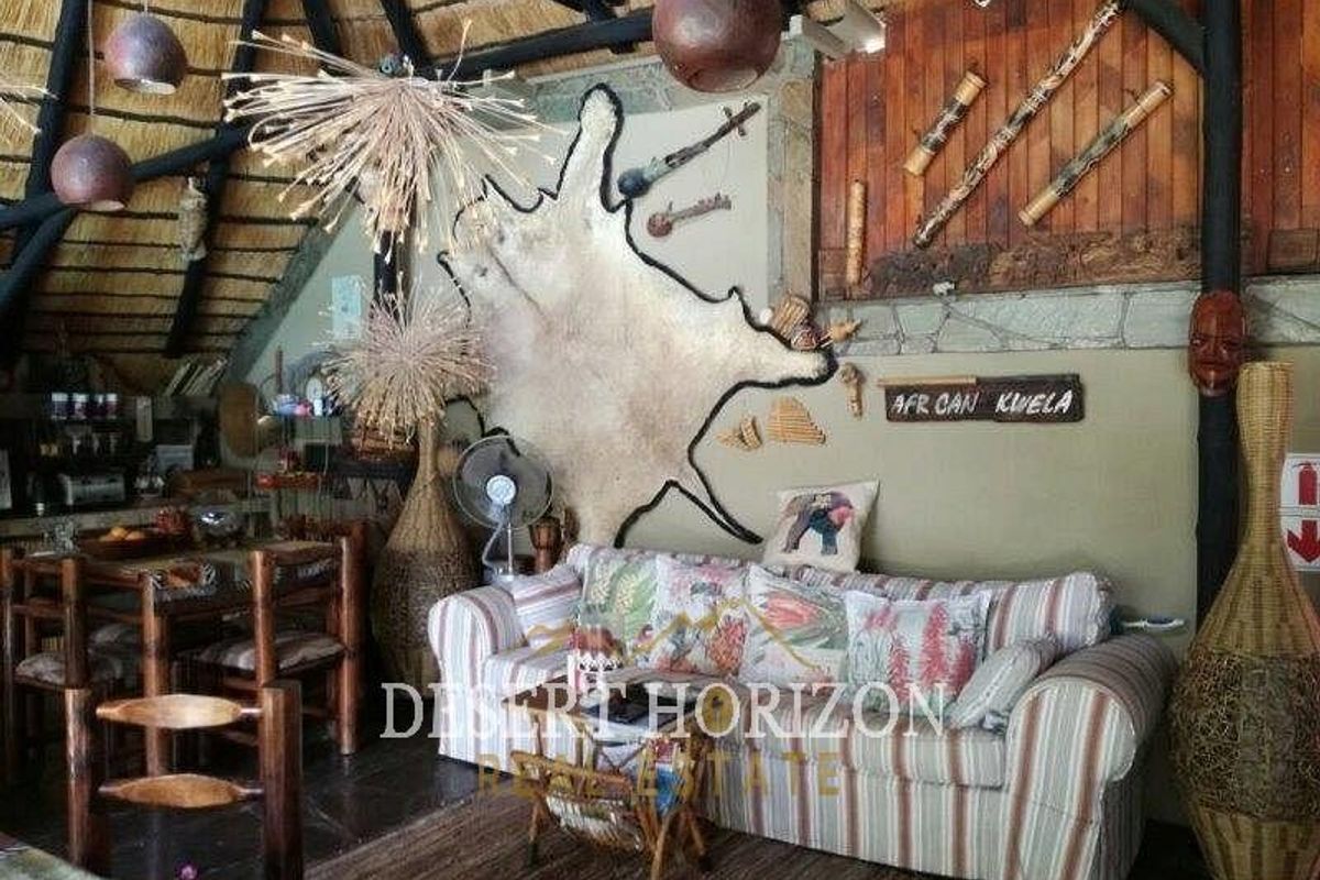 A rustic living area featuring a traditional thatched roof, exposed timber beams, and stone wall accents, creating a warm and authentic guest house atmosphere.