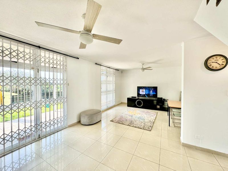 Bright living room featuring tiled flooring, ceiling fans, and large sliding glass doors with security gates providing access to the outdoor area.