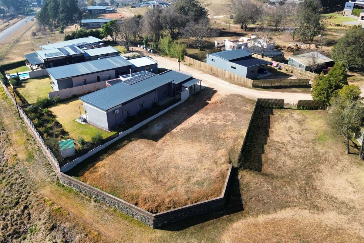 Aerial view of a vacant residential plot featuring a stone retaining wall, perimeter fencing, and access to a gravel road in a developed estate.