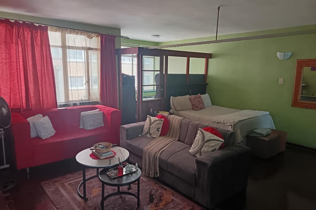 Open-plan studio apartment featuring timber flooring, a large window for natural light, and a built-in room divider separating the living and sleeping areas.