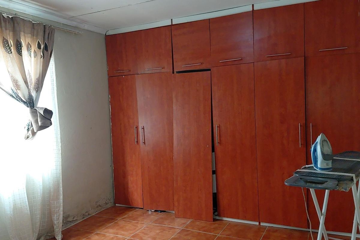 Bedroom featuring built-in wooden cupboards and tiled flooring, showing signs of wall dampness and minor maintenance requirements.