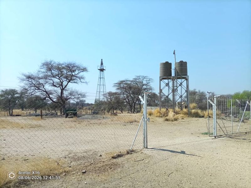 Outdoor area of the small holding featuring a steel water tank stand, windmill structure, and perimeter wire fencing.