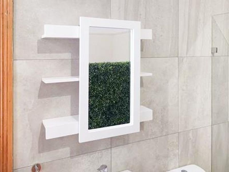 A modern bathroom featuring large format wall tiles, a glass shower screen, and a white wall-mounted mirror cabinet with integrated shelving.