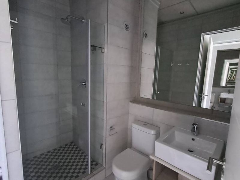 Modern bathroom featuring a glass-enclosed shower, wall-mounted toilet, vanity basin with storage cabinet, and a large mirror.