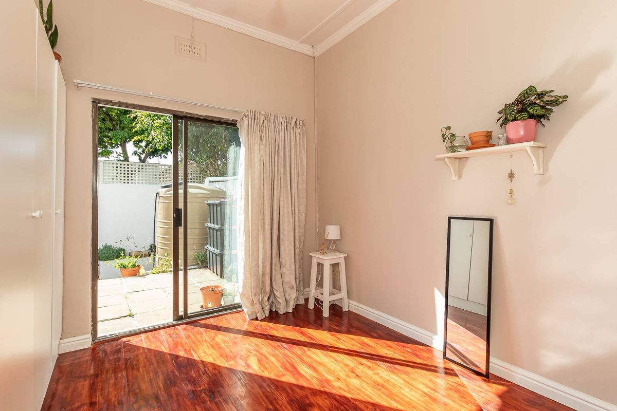 A bedroom featuring polished timber flooring, built-in wardrobe, and sliding glass doors providing direct access to a paved outdoor area.