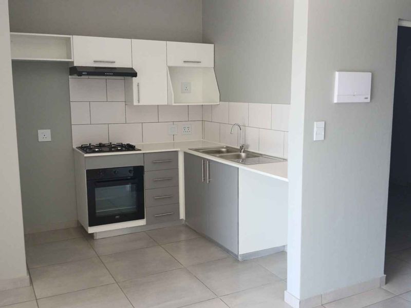 Modern kitchen featuring grey and white cabinetry, gas hob, electric oven, extractor fan, and tiled splashback in a clean, open-plan layout.
