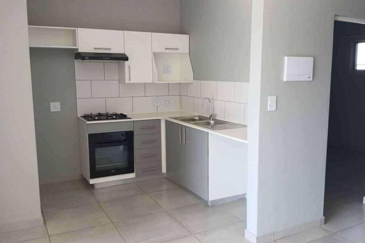 Modern kitchen featuring grey and white cabinetry, gas hob, electric oven, extractor fan, and tiled splashback in a clean, open-plan layout.