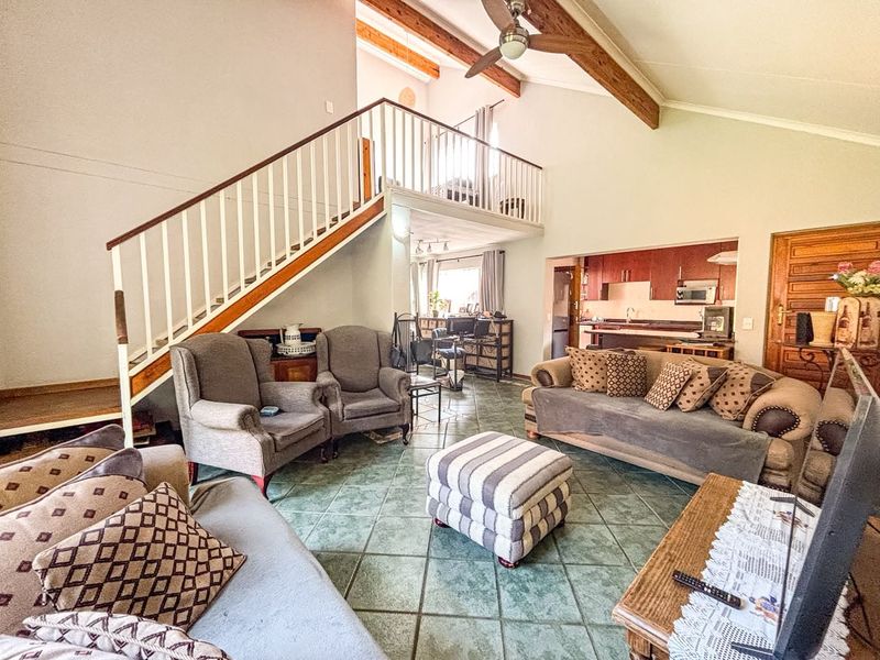 Spacious open-plan living area featuring a mezzanine level, exposed timber beams, tiled flooring, and an integrated kitchen space.