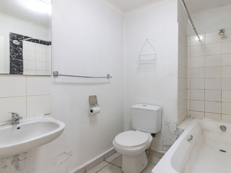 A dated bathroom featuring a pedestal basin, toilet, and bathtub with shower attachment, requiring cosmetic updates and wall repairs.