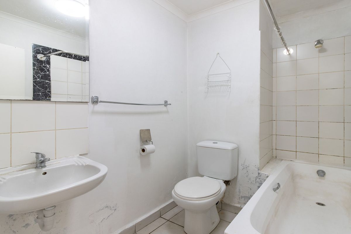 A dated bathroom featuring a pedestal basin, toilet, and bathtub with shower attachment, requiring cosmetic updates and wall repairs.