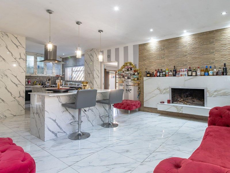 Spacious open-plan living and kitchen area featuring marble-look tiling, a central island, and a modern fireplace with stone-cladding detail.