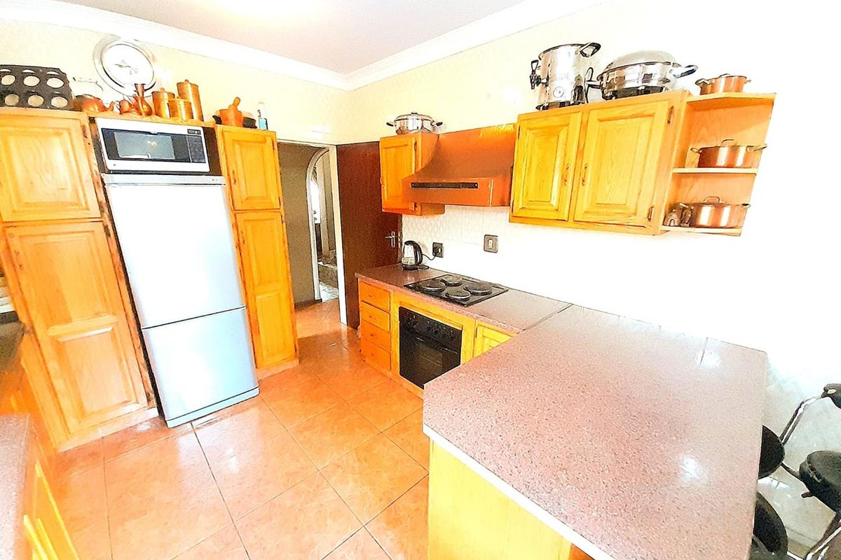 A functional kitchen featuring wooden cabinetry, a built-in oven, hob, extractor fan, and tiled flooring with a breakfast counter.