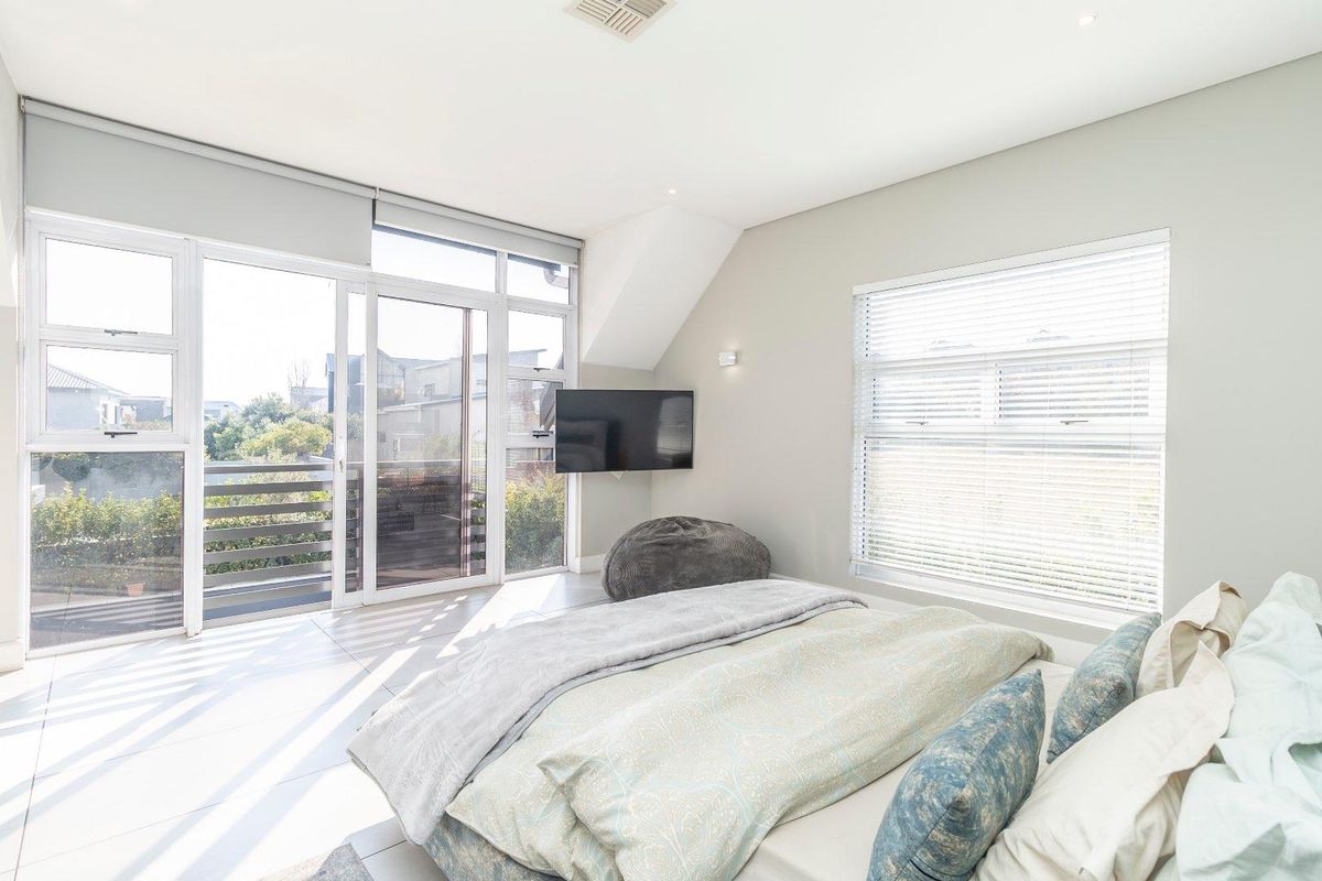 Bright and modern bedroom featuring large sliding glass doors leading to a balcony, tiled flooring, and neutral wall finishes.