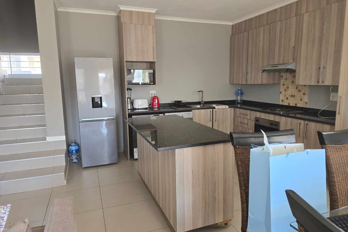 Modern kitchen featuring wood-finish cabinetry, granite countertops, a central island, and integrated appliances, adjacent to an internal staircase.
