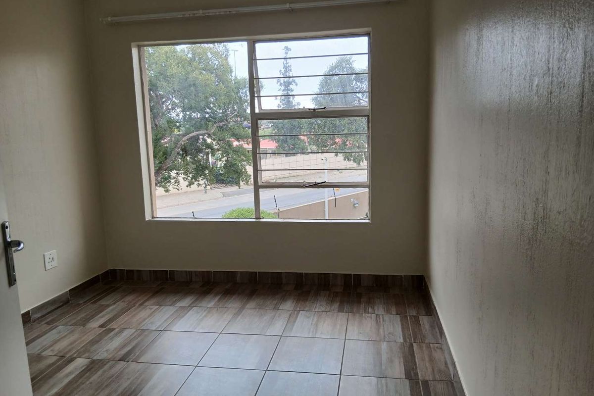 A bright, empty bedroom featuring tiled flooring, a large window with security bars, and neutral wall finishes.