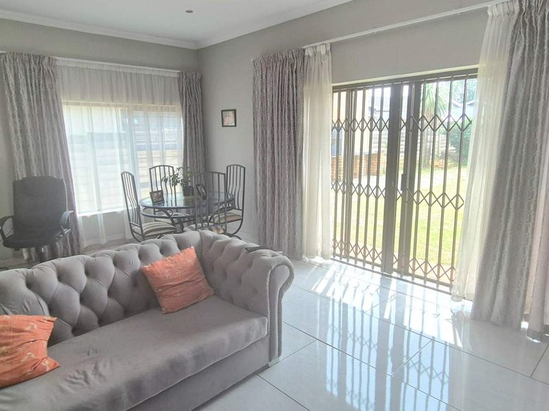 A bright living room featuring polished tiled flooring and a sliding glass door with a security gate, providing direct access to the garden.