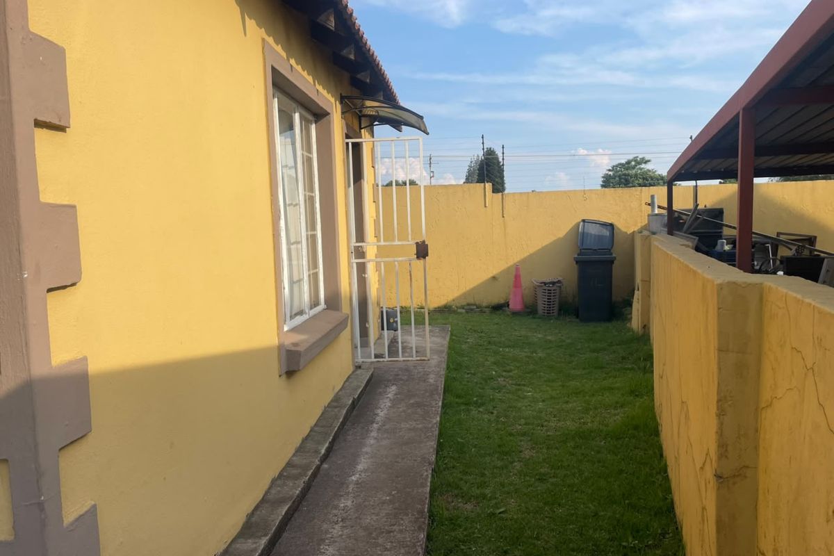 A rear exterior view showing a concrete pathway, security gate, and perimeter wall with visible signs of wear and maintenance needs.