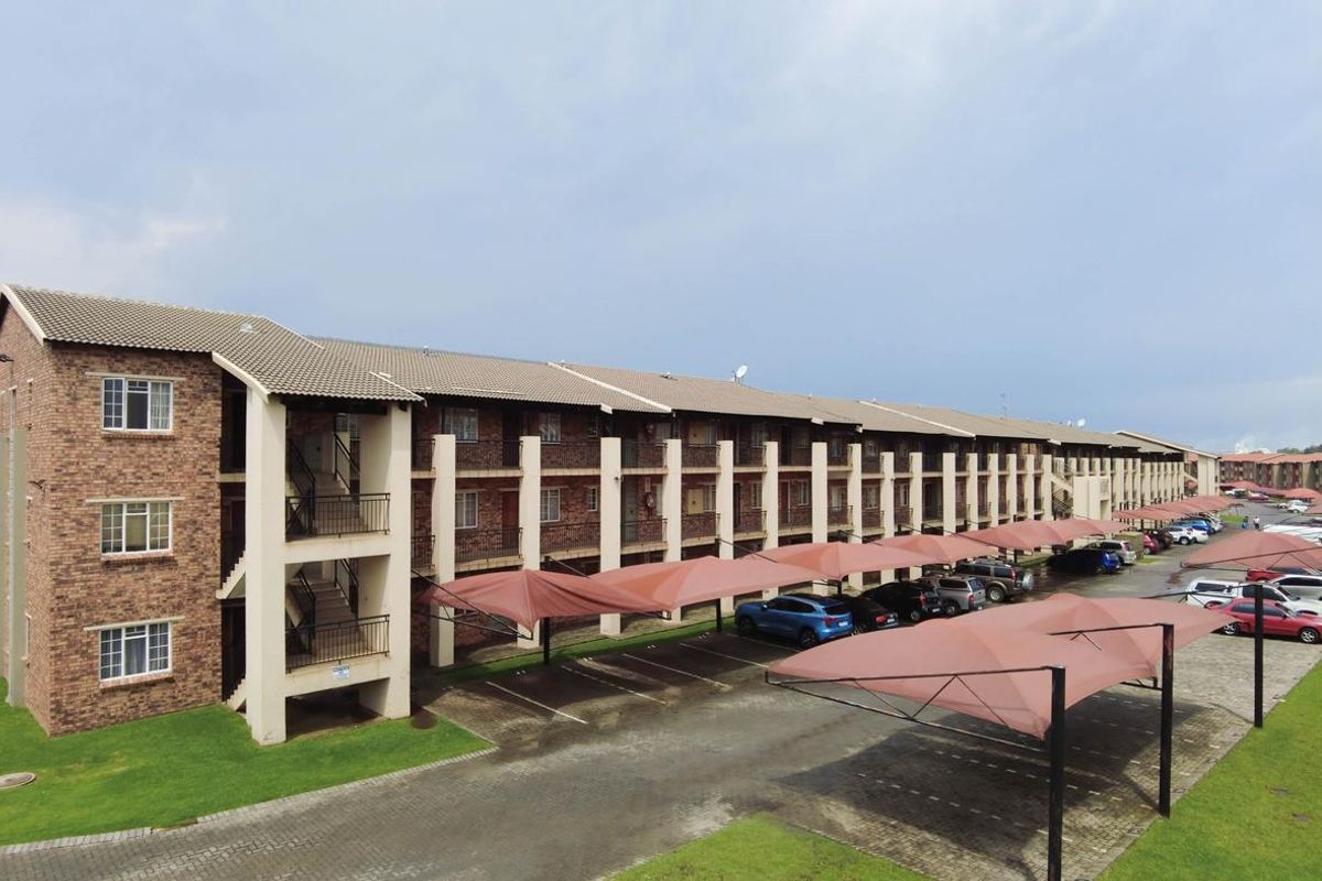 Aerial view of a multi-story apartment complex featuring brick facade, tiled roofing, and covered parking bays for residents.
