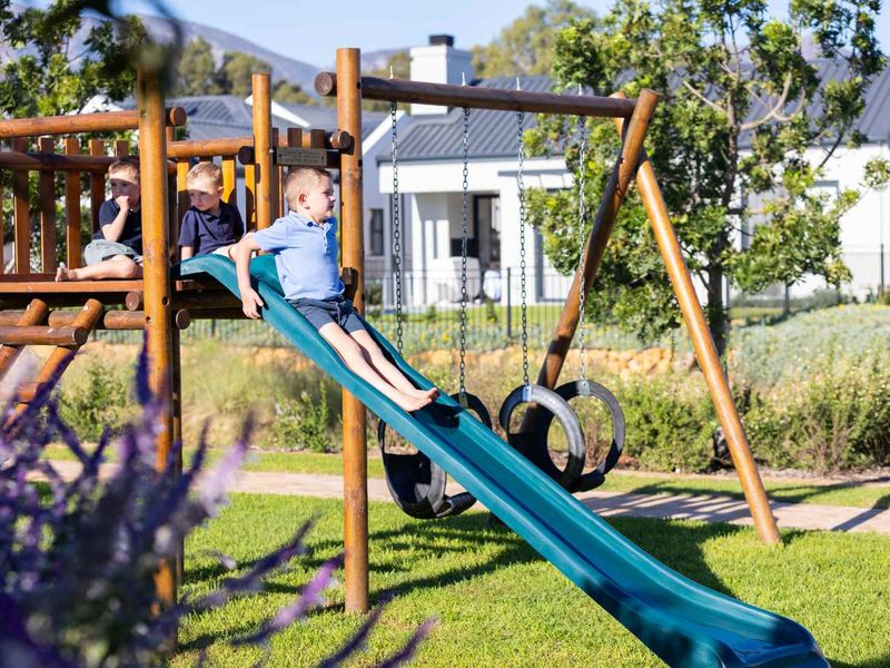 A well-maintained residential garden featuring a wooden playground structure with a slide and swing set, set against a landscaped lawn.