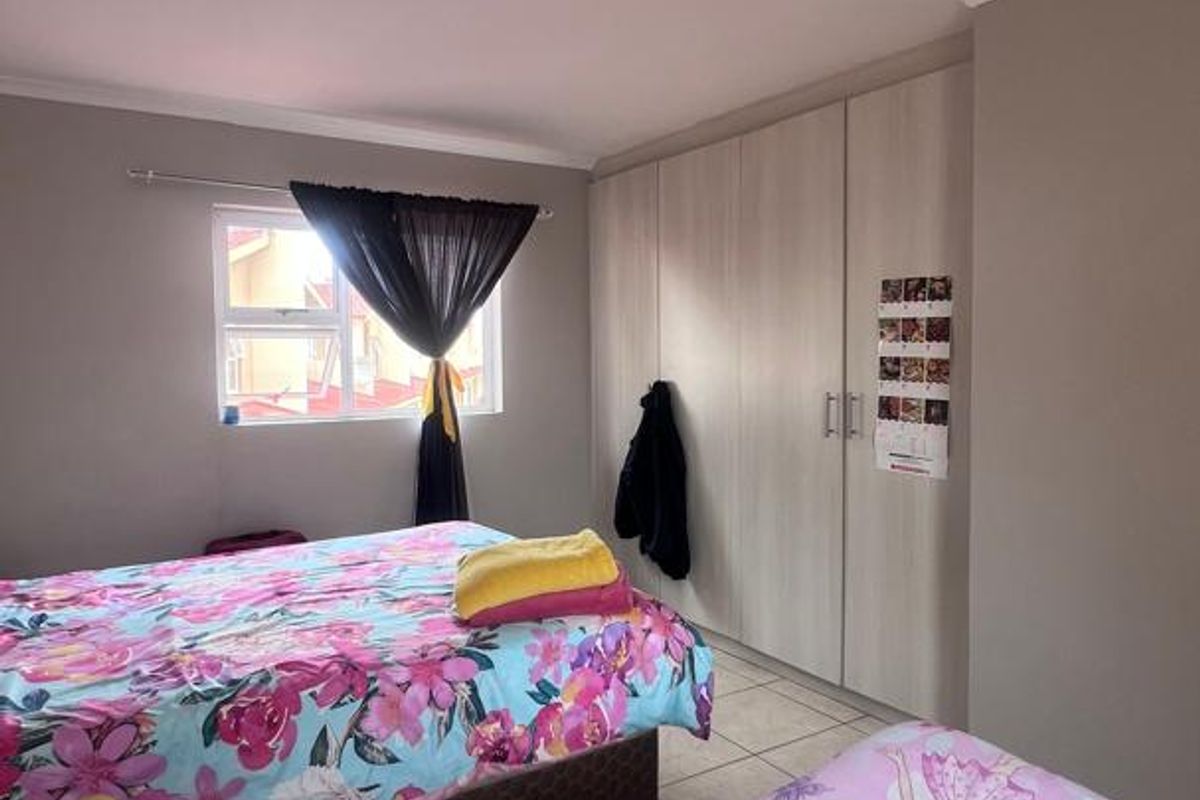 A bedroom featuring built-in cupboards with light wood-grain finish and tiled flooring.