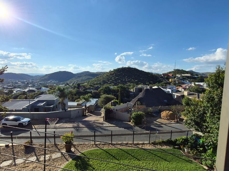 Elevated panoramic view overlooking the surrounding residential neighbourhood and distant hills, captured from a balcony with wire balustrade.
