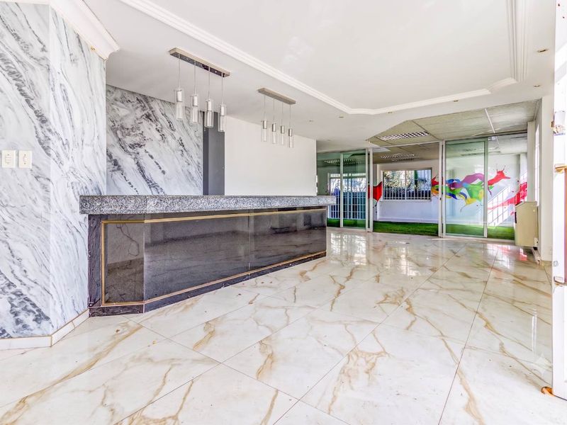 Spacious office bar area featuring marble-look flooring, a built-in service counter, and sliding glass partitions leading to an adjacent workspace.