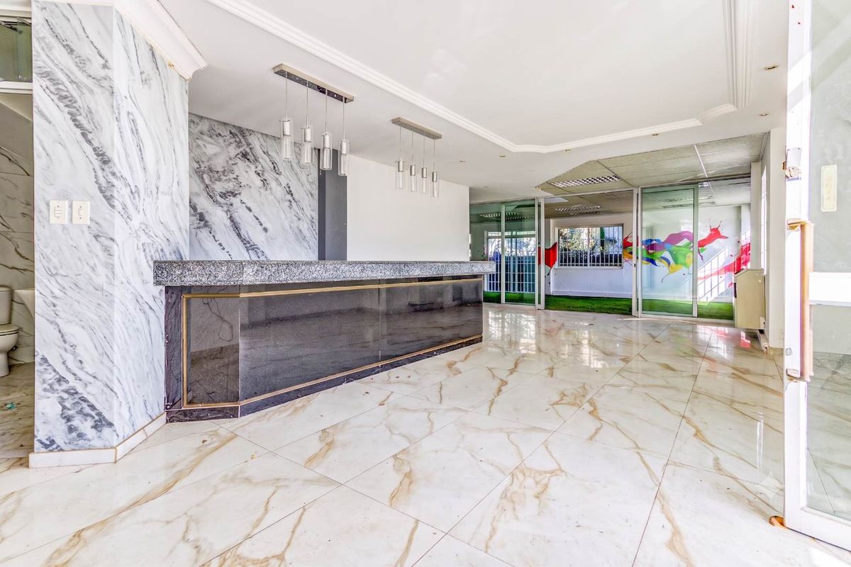 Spacious office bar area featuring marble-look flooring, a built-in service counter, and sliding glass partitions leading to an adjacent workspace.